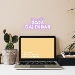 May include: A laptop displays a yellow screen with the text "I RADIATE ENERGY, BEAUTY, AND SELF-BELIEF." Above the laptop, the words "printable 2026 CALENDAR" are in a purple neon style. A cactus in a decorative pot sits to the left.