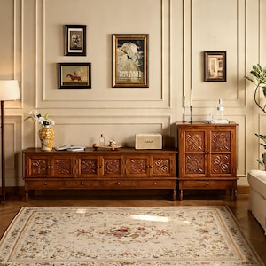 Pode incluir: Uma sala de estar com um móvel de entretenimento de madeira escura e um armário a condizer, ambos com desenhos florais esculpidos. A sala inclui um tapete creme com um padrão floral, obras de arte na parede e uma coluna Marshall.