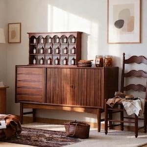 Op de afbeelding: Een donkerhouten kast met lades en een schuifdeur. Bovenop staan kleine bruine flesjes op een plank. Een bruine leren tas staat op de vloer. Een houten stoel staat ernaast.