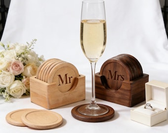 May include: A champagne flute with a drink, next to wooden coasters with "Mr" and "Mrs" engraved, and a ring in a box. The coasters are in wooden holders. A bouquet of flowers is in the background.