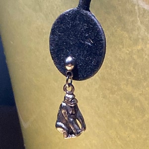 May include: Silver-toned monkey charm earring. The charm is a detailed miniature sculpture of a seated monkey. The earring is attached to a black, circular backing.