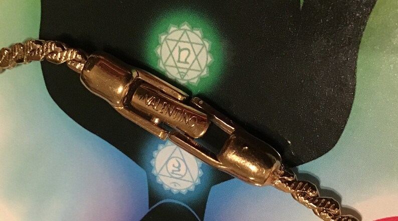 Puede incluir: Primer plano de un cierre de brazalete de cadena dorado con la palabra "VALENTINO" grabada.