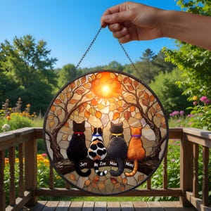 Puede incluir: Una vidriera redonda con cuatro gatos sentados en una rama, con una cálida escena de puesta de sol. Los gatos son negros, calicó, negros y naranjas, cada uno con un collar de diferente color. Los nombres están debajo.