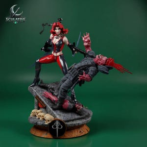 May include: A detailed figurine depicting a female character in a red and black costume, wielding a sword, and standing over a fallen figure. The base features skulls and a symbol, with the word "Sculative" visible.