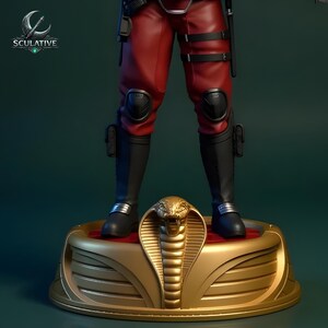 Puede incluir: Figura de acci&oacute;n detallada de un personaje con pantalones rojos, botas negras y rodilleras, de pie sobre una base dorada con tem&aacute;tica de cobra. La figura tiene un cintur&oacute;n negro y accesorios. La base es dorada con una parte superior roja.