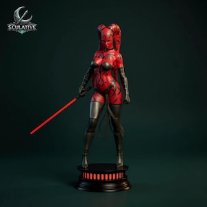 May include: A red and black statue of a female character holding a red lightsaber. The character has red skin with black markings, black clothing, and is standing on a black base. The logo "Sculative" is in the upper left corner.