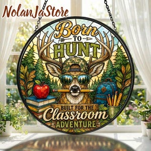Könnte beinhalten: Ein rundes Hängeschild im Buntglas-Stil mit einem Hirsch, der eine Camouflage-Kappe und eine Sonnenbrille trägt und einen Bleistift im Mund hält. Der Text lautet Born to HUNT und BUILT FOR THE CLASSROOM ADVENTURE, mit rotem Apfel, Büchern und Rucksack.