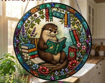 May include: Round stained glass window featuring a brown otter reading a book. The window is decorated with colorful books, flowers, and foliage. The text "Nolan JaStore" is at the top. The window is hanging from a chain.