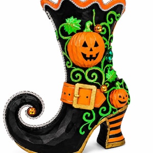 May include: A black boot-shaped decorative figurine featuring a curled toe, an orange buckled strap, and two carved jack-o'-lanterns. The design includes bright green vine accents, orange and black striped heels, and silver rhinestone trim along the edges.