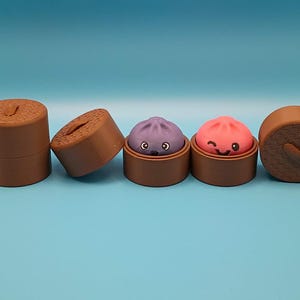 May include: A set of brown cylindrical containers with textured lids, two of which are open to reveal small, round, cartoon-faced figures. One figure is purple with a surprised expression, and the other is pink with a winking, smiling face.