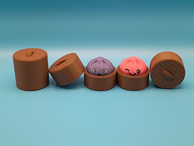 May include: A set of brown cylindrical containers with textured lids, two of which are open to reveal small, round, cartoon-faced figures. One figure is purple with a surprised expression, and the other is pink with a winking, smiling face.