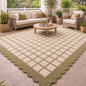 May include: An outdoor rug with a cream-colored grid pattern and a scalloped olive green border. The rug is placed on a tiled patio, with wicker furniture and potted plants in the background. The scene evokes a relaxed, inviting atmosphere.