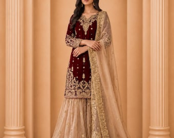 May include: A formal maroon velvet outfit with gold embroidery. The long-sleeved top and flared pants are adorned with intricate gold patterns. A sheer, beige shawl with gold trim completes the ensemble. The outfit is suitable for special occasions.