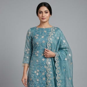 Peut inclure: Un ensemble salwar kameez de couleur sarcelle. La tenue comprend un haut à manches longues et un pantalon salwar assorti, tous deux ornés de broderies argentées. Un dupatta transparent avec des bords festonnés complète l'ensemble. La tenue est ornée de franges.