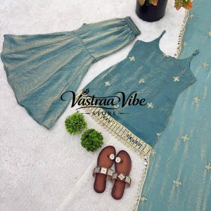 May include: A teal sleeveless top with spaghetti straps and gold embroidery, paired with matching flared trousers and a long dupatta. The top features a gold-trimmed hem with hanging beads. A pair of brown flat sandals are placed nearby.