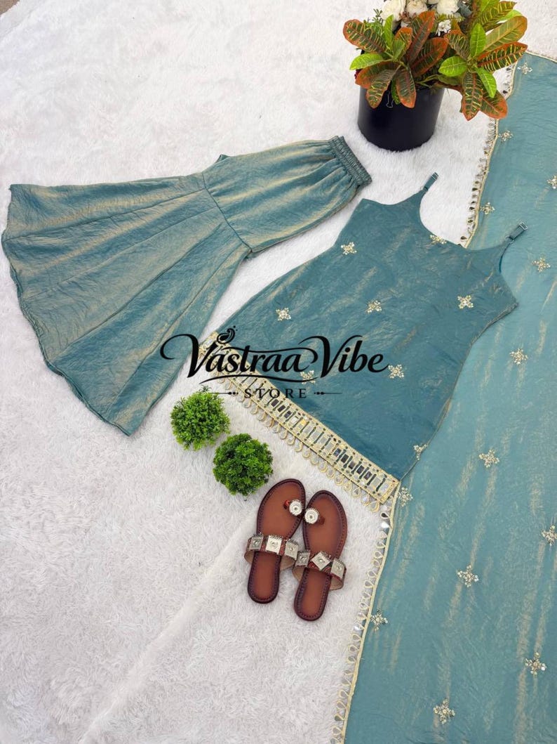 May include: A teal sleeveless top with spaghetti straps and gold embroidery, paired with matching flared trousers and a long dupatta. The top features a gold-trimmed hem with hanging beads. A pair of brown flat sandals are placed nearby.