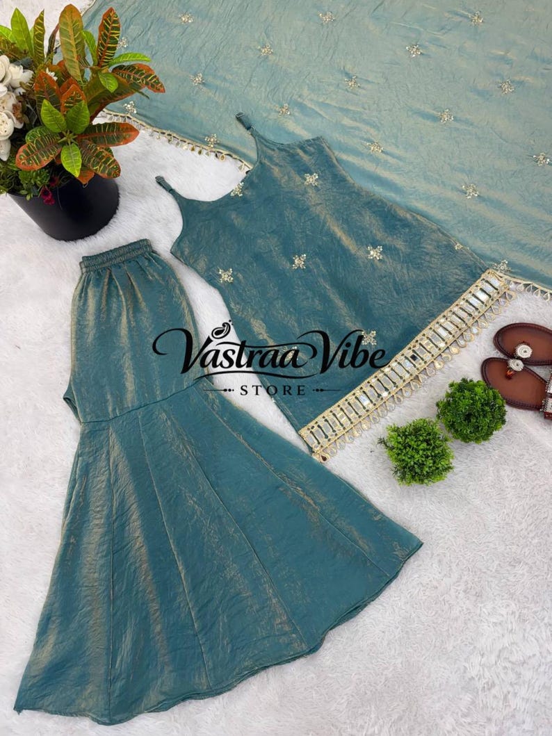 May include: A teal sleeveless top with thin straps, matching flared pants, and a coordinating dupatta, all featuring small gold floral embroidery. The top hem is decorated with a gold fringe trim. The text Vastraa Vibe STORE is visible.