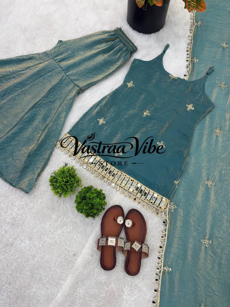 May include: A teal sleeveless top with thin straps, matching wide-leg pants, and a long scarf, all featuring gold embroidery and mirror accents. The top displays the text Vastraa Vibe Store. A pair of brown flat sandals with metallic embellishments.