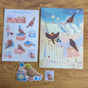 以下が含まれることがあります： 「Blueberry Crow」と書かれたステッカーシート、長方形のアートプリント、そして茶色の鳥、ブルーベリー、物干しロープに干された洗濯物、ジャムの瓶、フェンスが描かれた2枚のステッカー。背景は黄色い星が輝く青い空です。