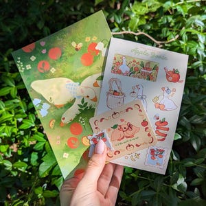 Könnte beinhalten: Ein Set aus Schreibwaren mit Apple Goose-Motiv, bestehend aus einem großen illustrierten Druck, einem Stickerbogen mit verschiedenen Gänse- und Apfeldesigns sowie einer kleinen quadratischen Karte mit dem Text U r the apple of my eye.