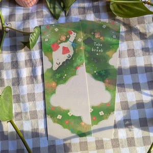 Op de afbeelding: Twee geïllustreerde bladwijzers met een grillig ontwerp. Eén bladwijzer toont een witte gans met rode accenten en een blauwe strik, tegen een groene weide met bloemen. De andere bladwijzer heeft de tekst "Take a break".