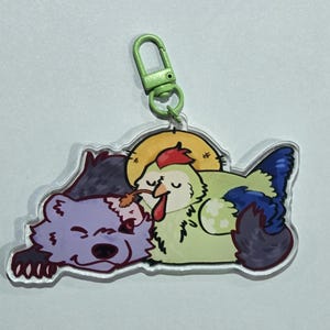 May include: A clear acrylic keychain featuring a cartoon bear and chicken. The bear is purple, and the chicken is light green with blue and red accents. A green clasp is attached to the top. The design is whimsical and colorful.