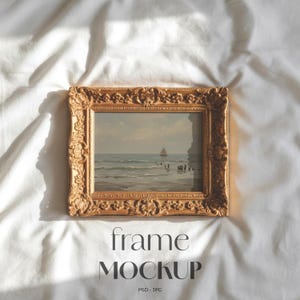 May include: A gold-colored, ornate picture frame with a landscape painting of a seascape. The frame is square with detailed carvings. The text "frame MOCKUP" is at the bottom of the image.