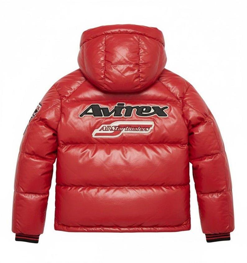 May include: A red puffer jacket with a hood. The jacket features the brand name "Avirex" in white and black lettering across the back, with "All Star Dualers" below. The jacket has black and red striped cuffs.