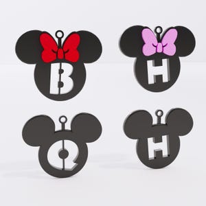 May include: Four black Mickey Mouse head-shaped ornaments with white letters and bows. One has a red bow and the letter "B", another has a pink bow and the letter "H", and the others have the letters "Q" and "H".