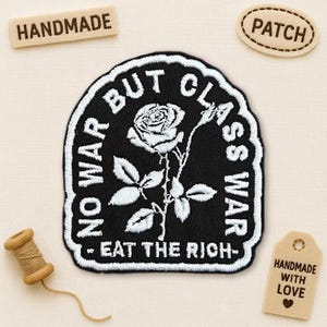 May include: Black and white embroidered patch with a rose design and the text "NO WAR BUT CLASS WAR - EAT THE RICH-". Includes small wooden tags that say "HANDMADE" and "PATCH". Also includes a wooden spool of thread.