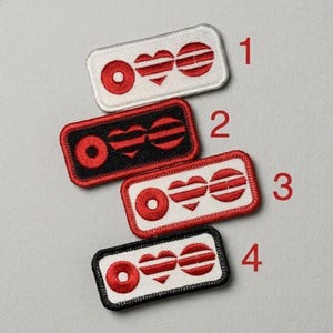 May include: Four embroidered patches with a red and white design. Each patch features a circle, a heart, and a striped circle. The patches have different colored borders: white, black, and red. The patches are rectangular.