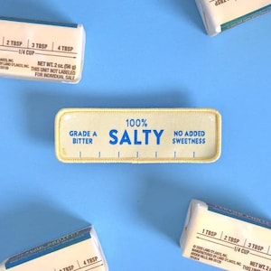 May include: A white ceramic mug with a black handle and the text "But First, Coffee" in a black, handwritten-style font. The mug is on a white surface.