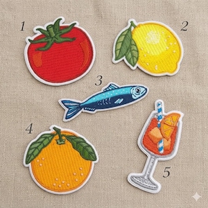 May include: Embroidered patches featuring a red tomato, yellow lemon, blue fish, orange, and a cocktail with an orange slice. Each patch has a white border and is designed with detailed stitching. These patches are ideal for adding flair to clothing or accessories.