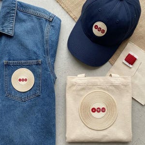 May include: A white ceramic mug with a black handle and the text "But First, Coffee" in a bold, black font. The mug is set against a blurred background, suggesting a cozy setting.