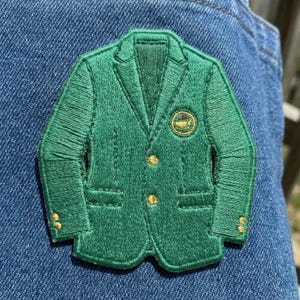 May include: Embroidered green blazer patch with gold buttons and a circular emblem. The patch is a detailed representation of a classic blazer, perfect for adding a touch of style to clothing or accessories.