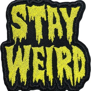 May include: Embroidered patch with the words "STAY WEIRD" in yellow, dripping-style lettering on a black background. The patch has a black border and is likely designed to be sewn or ironed onto fabric.