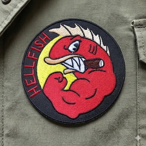 May include: Embroidered patch featuring a red cartoon fish with a cigar, flexing its bicep. The patch has the word "HELLFISH" in red letters around the edge, set against a black background with a yellow crescent.