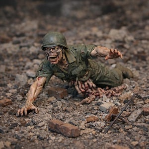 Puede incluir: Figura detallada de un soldado zombi arrastrándose sobre una superficie cubierta de escombros. La figura lleva un uniforme y casco militar verde, con carne y órganos internos expuestos. El zombi tiene una expresión amenazante.