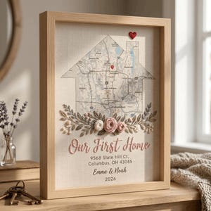 May include: A framed wall art piece featuring a house-shaped map of Columbus, Ohio, with a red heart pin. Below the map are embroidered flowers, the text "Our First Home", the address 9568 Slate Hill Ct, Columbus, OH 43085, Emma & Noah, and 2026.