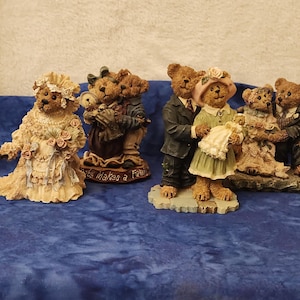 May include: A collection of bear figurines depicting various wedding and family scenes. The bears are dressed in wedding attire, with one bear in a bridal gown and others in suits and dresses. The figurines are on a blue surface.
