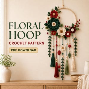 May include: A wall hanging featuring a wooden hoop decorated with crocheted red, dark green, and cream flowers, leaves, and berries, with hanging strands of beads, leaves, and tassels. Text reads: FLORAL HOOP CROCHET PATTERN PDF DOWNLOAD.