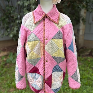 May include: A quilted jacket featuring a patchwork design of pink, yellow, blue, and white fabric squares. The garment has a collared neckline, long sleeves, and a front button closure with a patterned trim along the edges and the center placket.