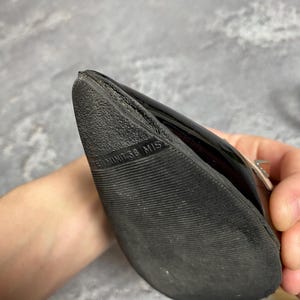 May include: Black patent leather shoe with a textured sole. The shoe's sole has the text "TERMINIT 38 MIS". The shoe is held by a person.