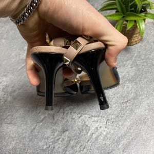 May include: A pair of black and beige high-heeled sandals with gold-colored stud accents. The sandals have a slingback design and a pointed toe. The heels are approximately 4 inches tall.