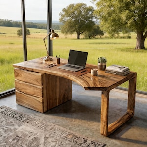 May include: A solid wood desk with a natural edge design. The desk features a built-in drawer unit and a curved leg. A laptop, lamp, and accessories sit on the desk. The desk is in front of a large window with a view of a green field.