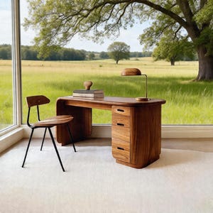 May include: A wooden desk with three drawers and a matching chair. A small wooden lamp and a stack of books sit on the desk. The chair has a black metal frame. The desk and chair are in front of a large window overlooking a green field.