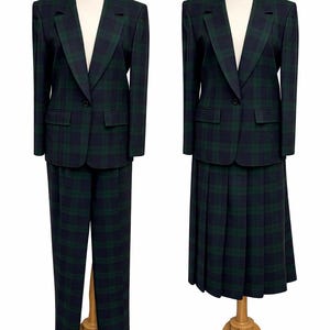 May include: Two-piece plaid suit in navy blue and green. One suit features trousers, the other a pleated skirt. Both have a single-button blazer with notched lapels and front pockets. The suits are displayed on mannequins.