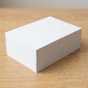 Op de afbeelding: Een dikke, rechthoekige stapel van effen witte vellen papier. De stapel is netjes uitgelijnd en vormt een solide blok met scherpe, strakke randen. Elk vel is ondoorzichtig en helderwit, wat zorgt voor een uniforme uitstraling van de stapel.