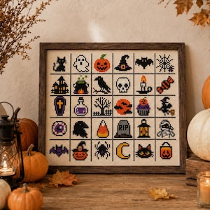Pode incluir: Um mostruário de ponto cruz emoldurado apresentando uma grade de trinta pequenos ícones com tema de Halloween, incluindo um gato preto, fantasma, abóbora, chapéu de bruxa, morcego, teia de aranha, casa assombrada, caldeirão, corvo, caveira, vela, doce, caixão, poção, árvore, lua, cupcake, bruxa, olho, corvo, doce de milho, lápide, lanterna, múmia, morcego, abóbora de Halloween, aranha, lua crescente, rosto de gato e balde de abóbora.