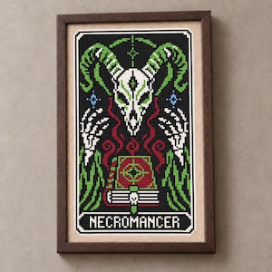 May include: A framed cross-stitch embroidery featuring a white horned skull, skeletal hands, and a red book with a skull icon. The design is set against a black background with green accents and the word NECROMANCER stitched in white at the bottom.